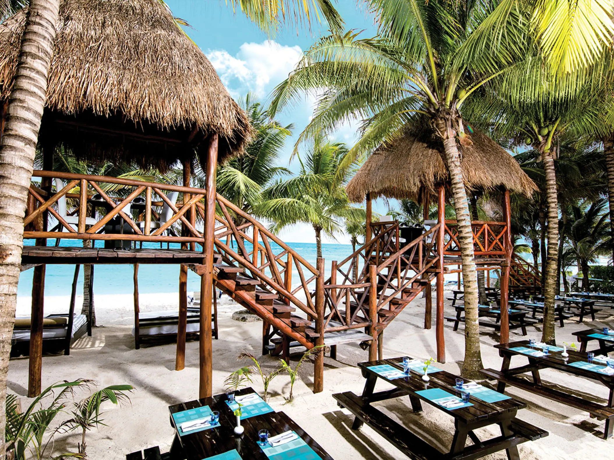 Thatched-roof beach cabins and dining tables at El Dorado Seaside Suites, Riviera Maya