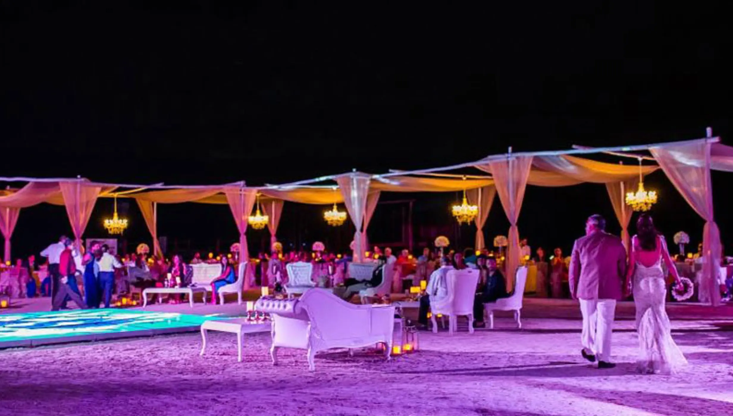 Beachfront wedding reception at night with lit dance floor and chandeliers at El Dorado Maroma, Riviera Maya