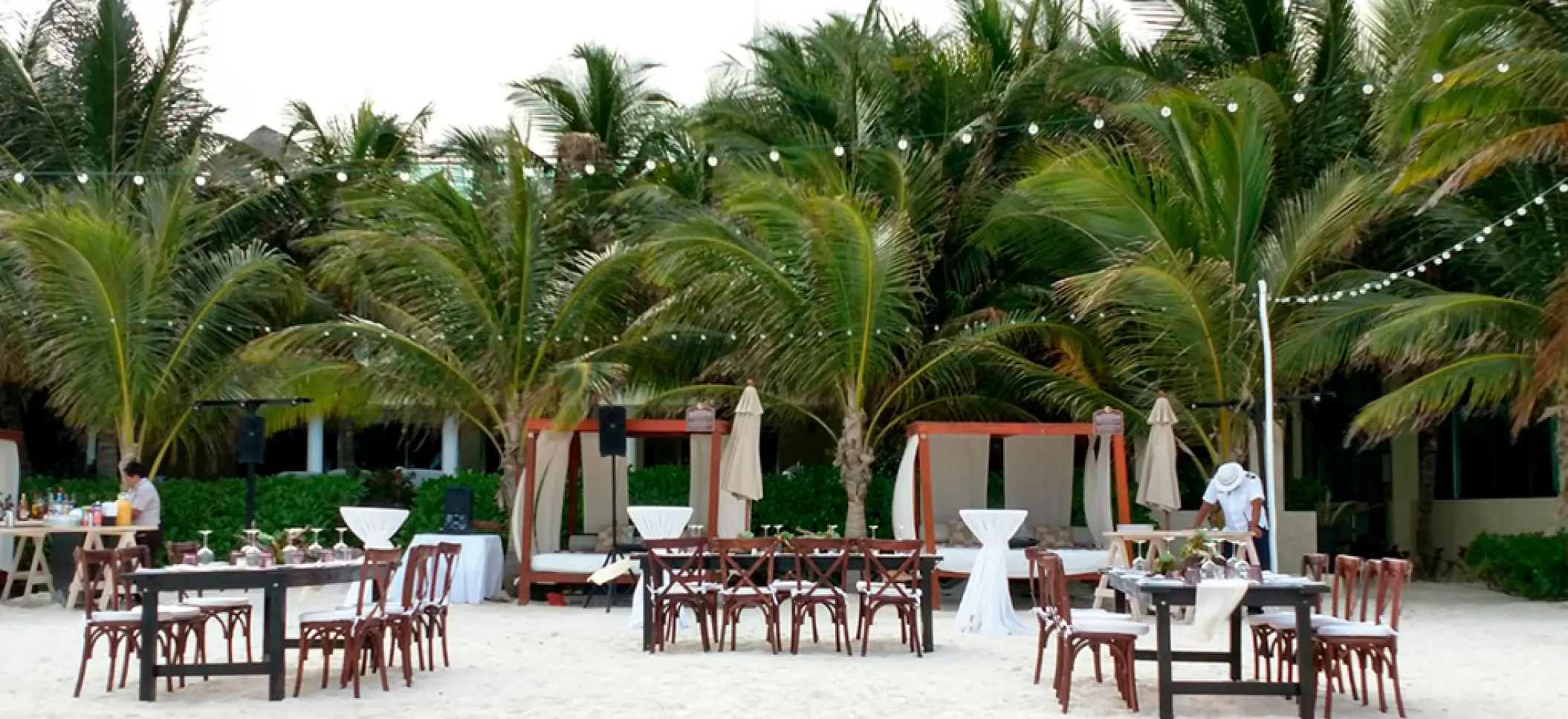 Beachfront wedding reception with wooden tables and string lights at El Dorado Maroma, Riviera Maya