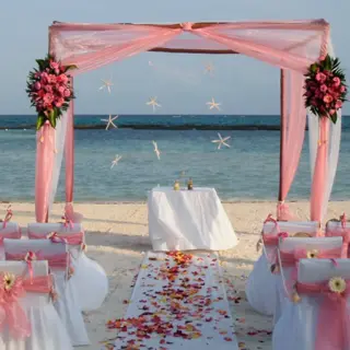 Beachfront wedding ceremony setup with pink draped huppah at El Dorado Maroma, Riviera Maya