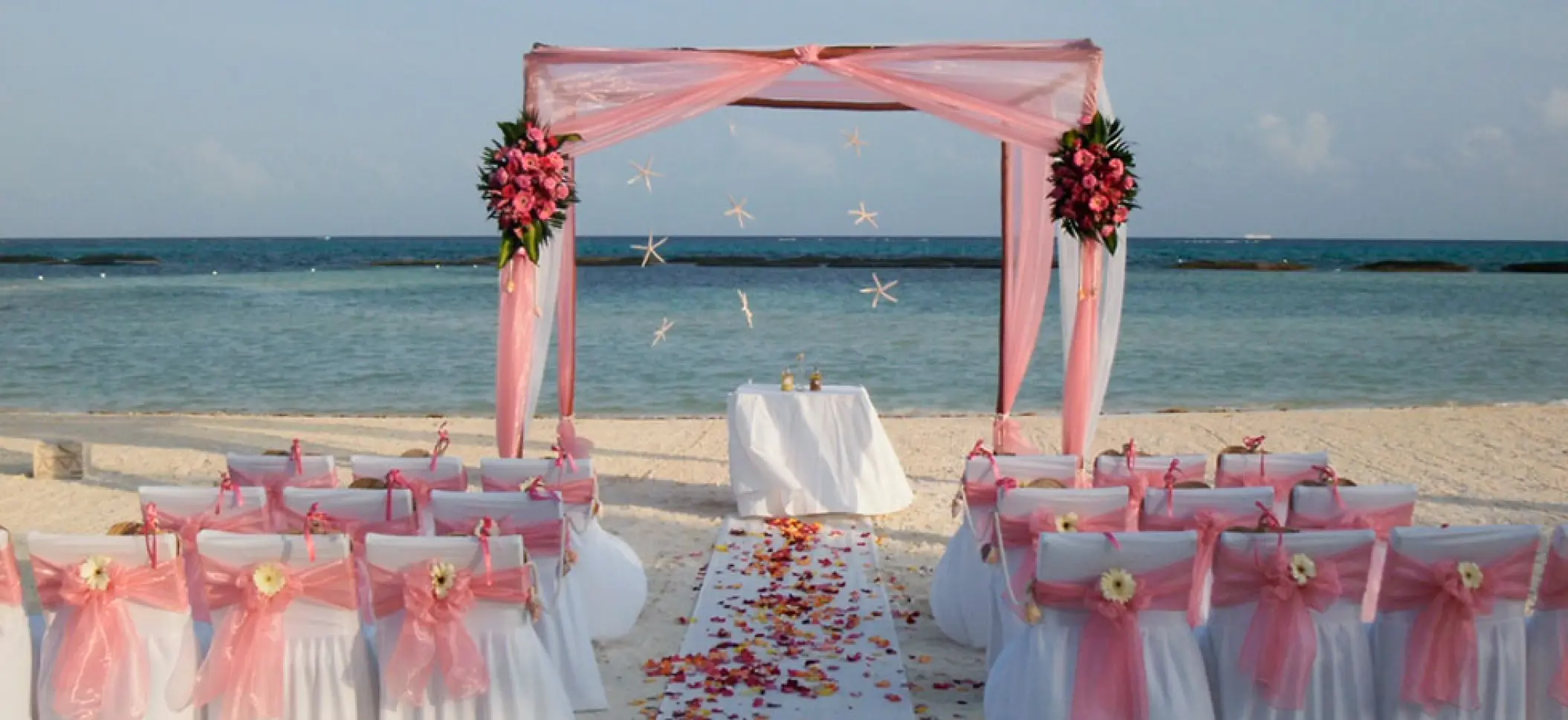 Beachfront wedding ceremony setup with pink draped huppah at El Dorado Maroma, Riviera Maya