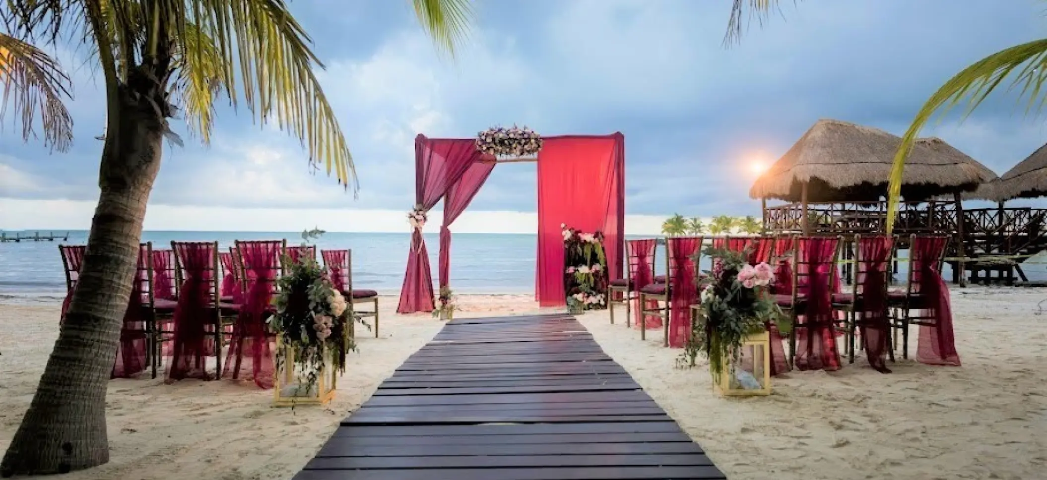 Beachfront wedding ceremony setup with pink draped arch and wooden aisle at El Dorado Maroma, Riviera Maya
