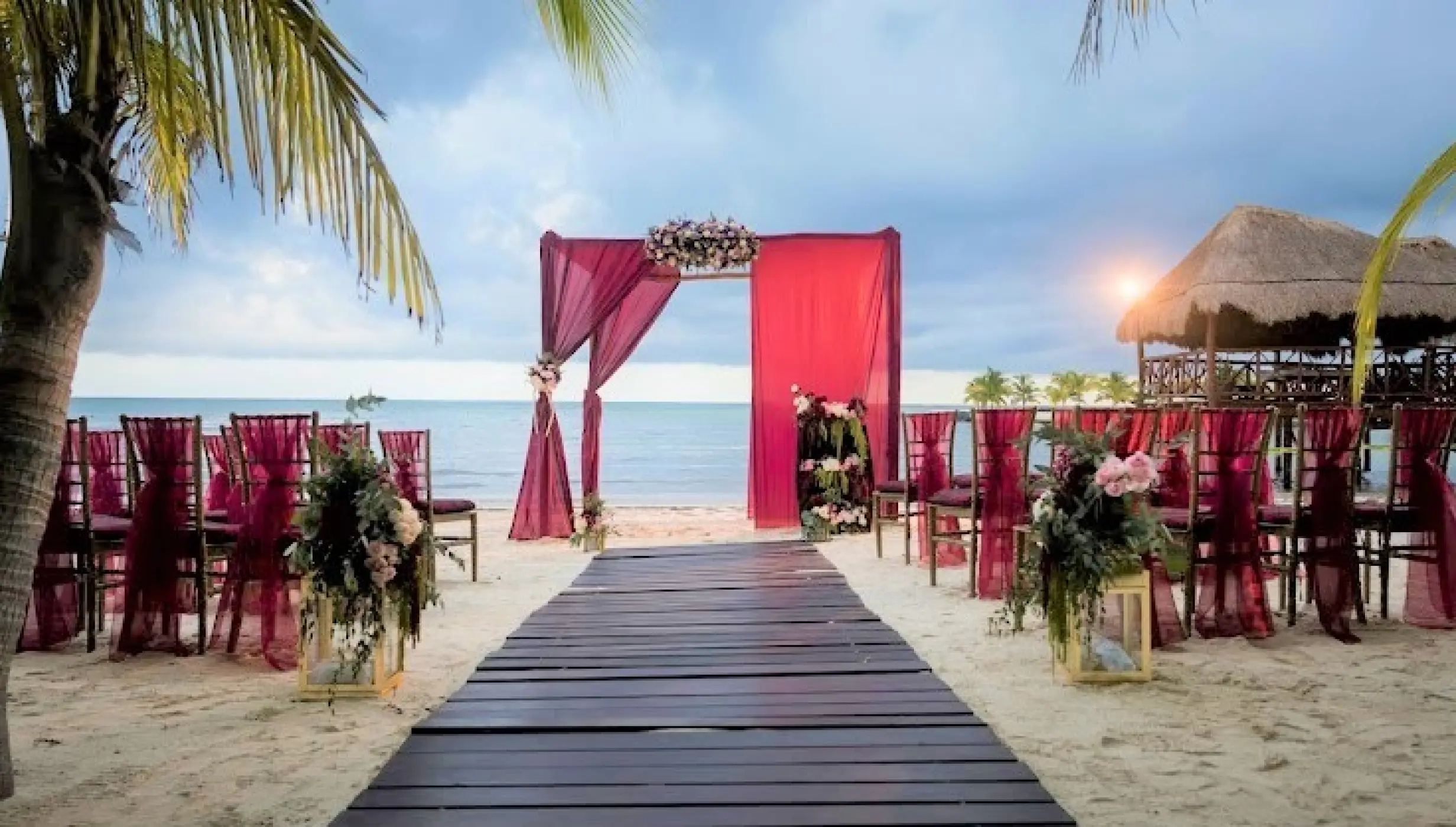 Beachfront wedding ceremony setup with pink draped arch and wooden aisle at El Dorado Maroma, Riviera Maya