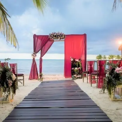 Beachfront wedding ceremony setup with pink draped arch and wooden aisle at El Dorado Maroma, Riviera Maya