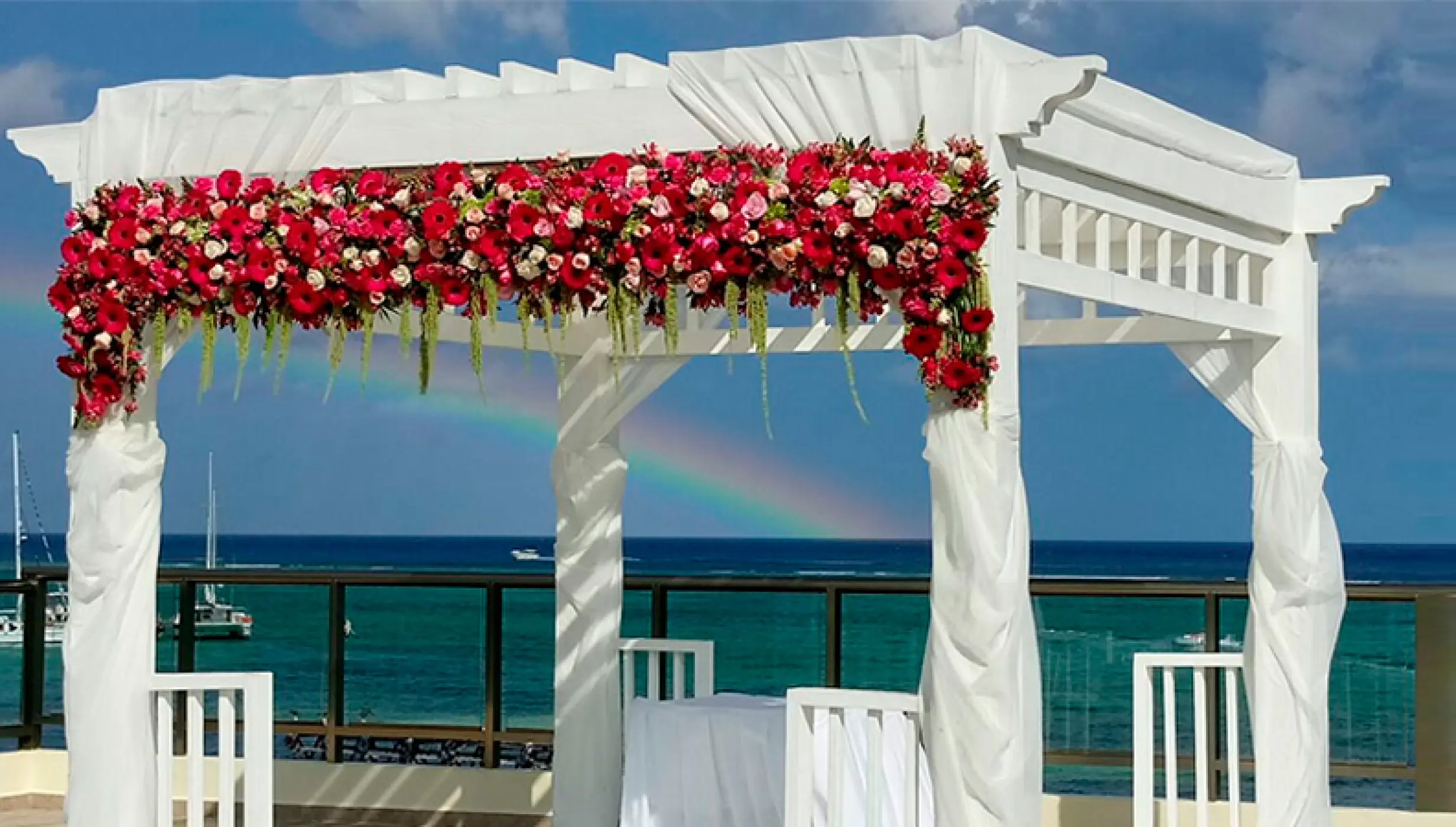 Sky deck wedding ceremony gazebo with red flowers and a rainbow at El Dorado Maroma, Riviera Maya