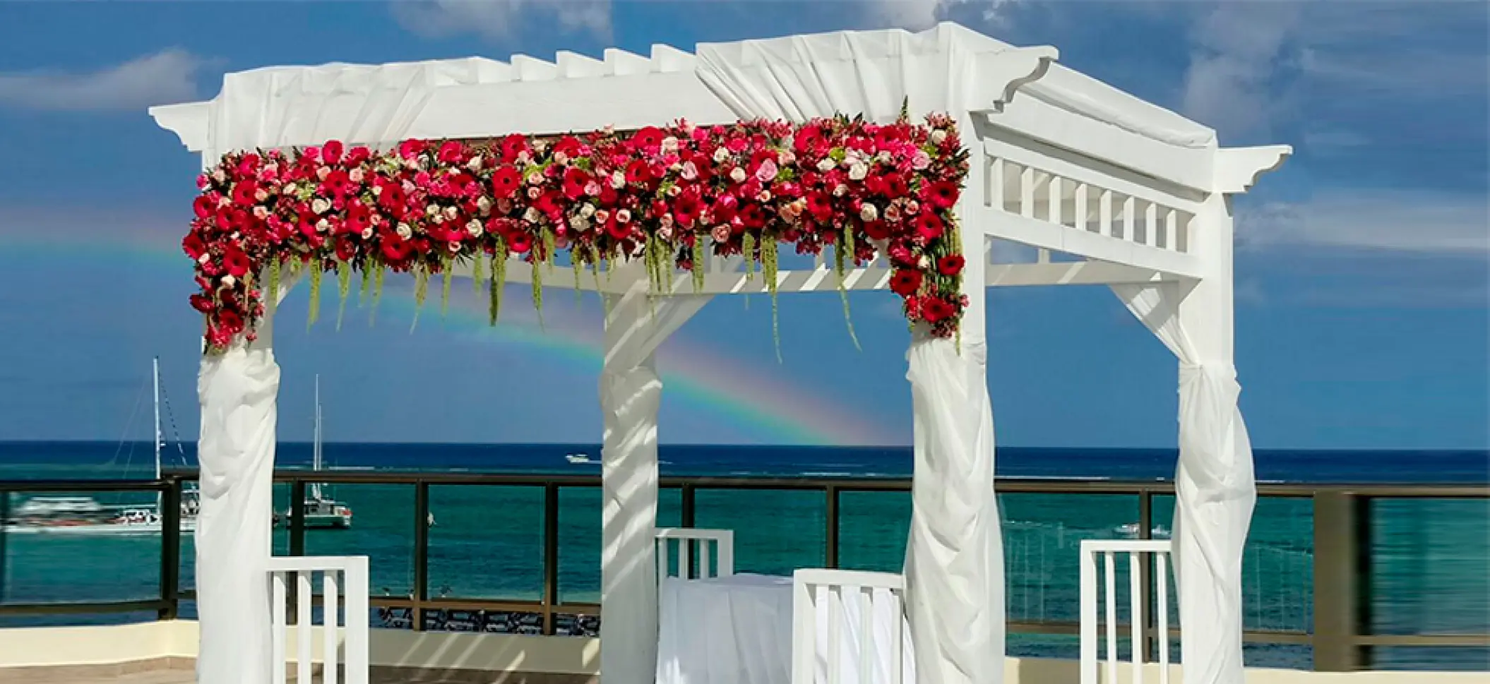 Sky deck wedding ceremony gazebo with red flowers and a rainbow at El Dorado Maroma, Riviera Maya