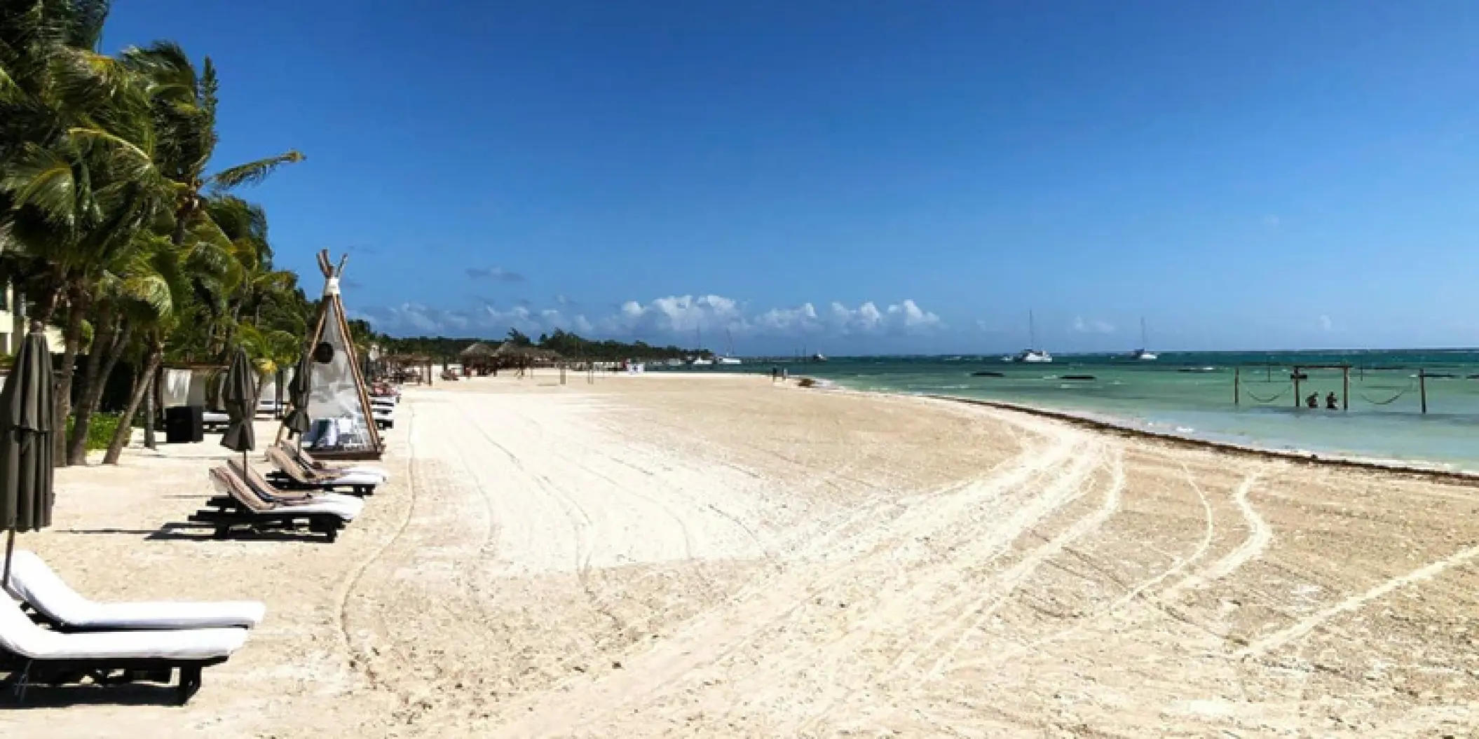 White sand beach with lounge chairs and palm trees at El Dorado Maroma, Riviera Maya