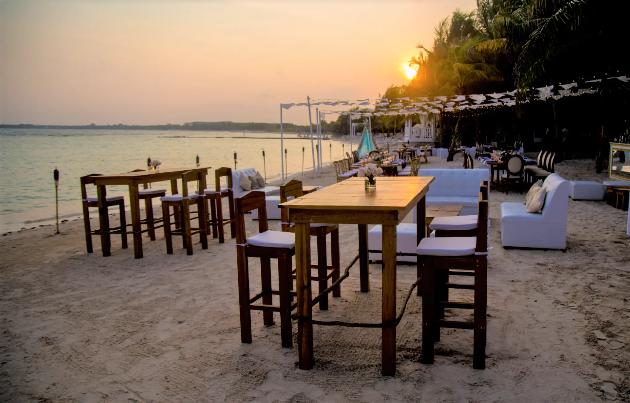 Beachfront wedding reception tables and white lounge seating at sunset at El Dorado Seaside Palms, Riviera Maya