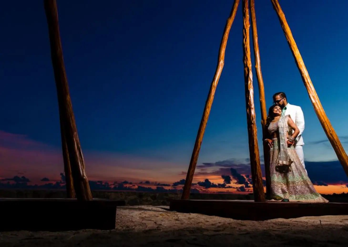 Newlyweds posing under a wooden structure at sunset at El Dorado Seaside Palms, Riviera Maya