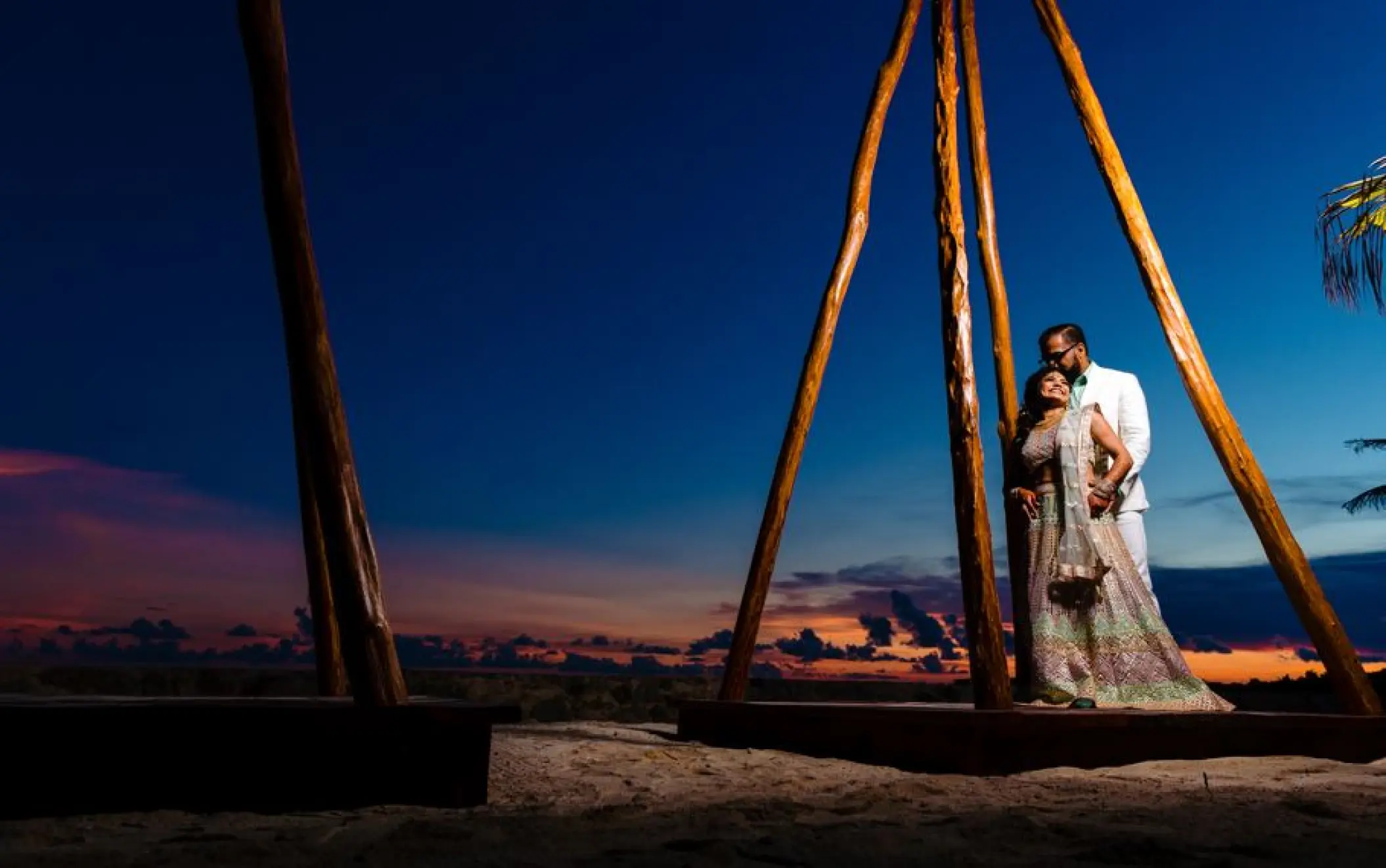 Newlyweds posing under a wooden structure at sunset at El Dorado Seaside Palms, Riviera Maya