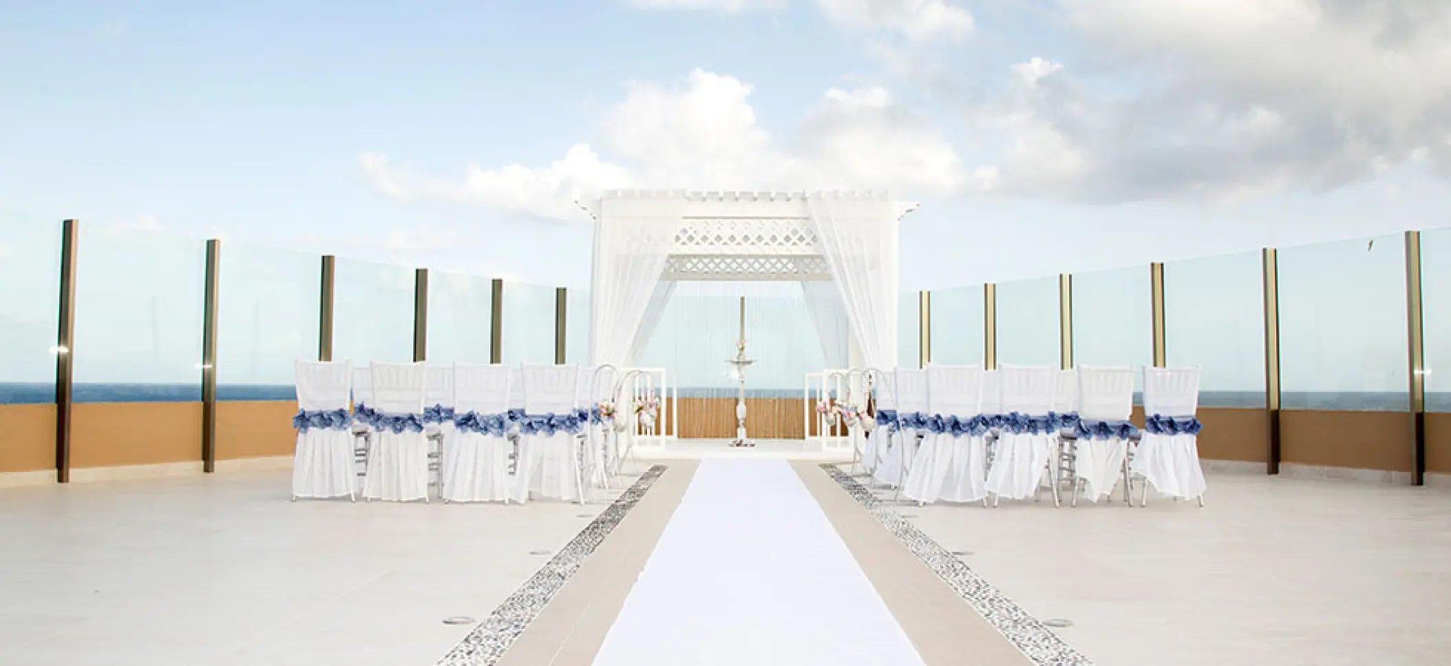 Sky deck wedding ceremony with white gazebo and blue-ribboned chairs at El Dorado Seaside Palms, Riviera Maya