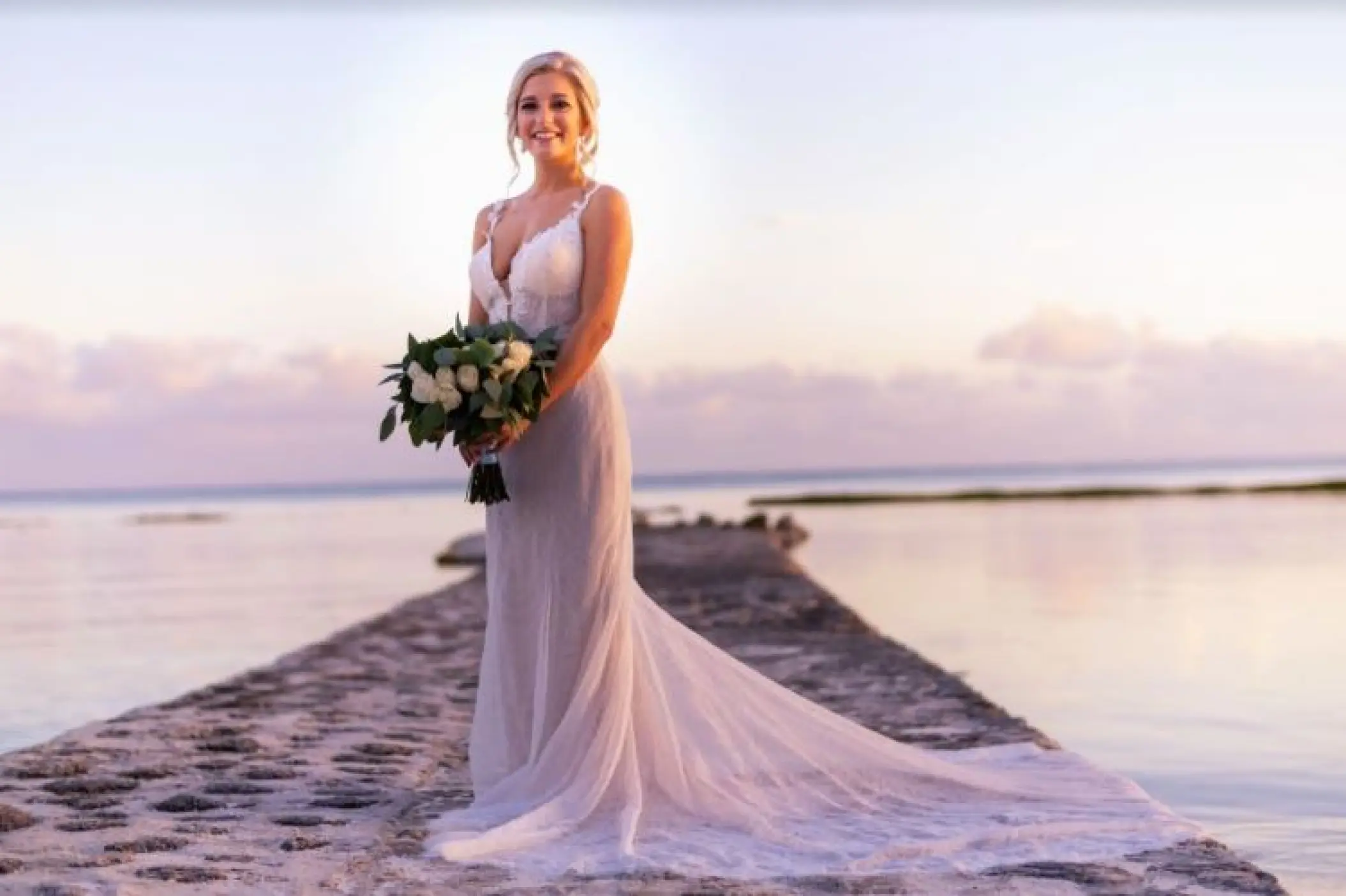 Bride holding a bouquet on a stone pier during sunset at El Dorado Seaside Palms, Riviera Maya