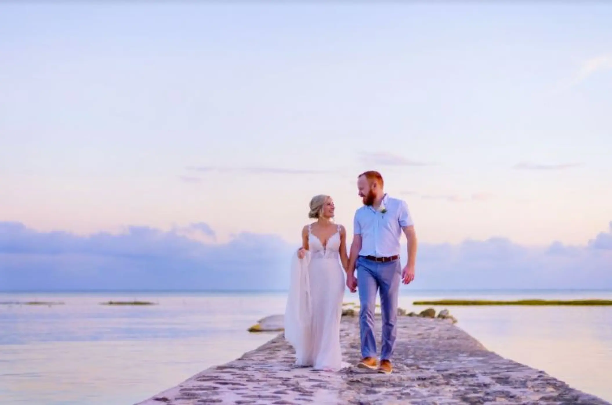 Bride and groom walking along a stone pier at sunset at El Dorado Seaside Palms, Riviera Maya