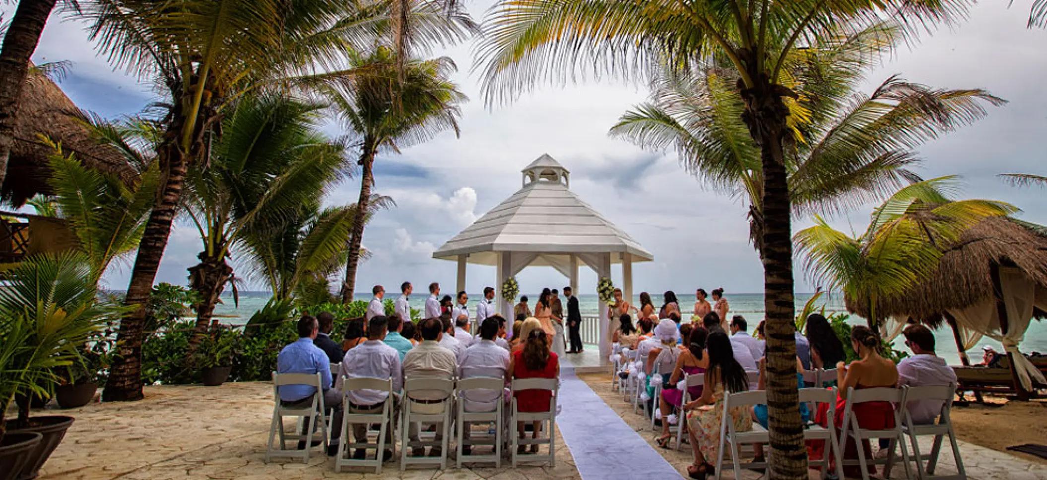White gazebo wedding ceremony framed by palm trees at El Dorado Seaside Palms, Riviera Maya