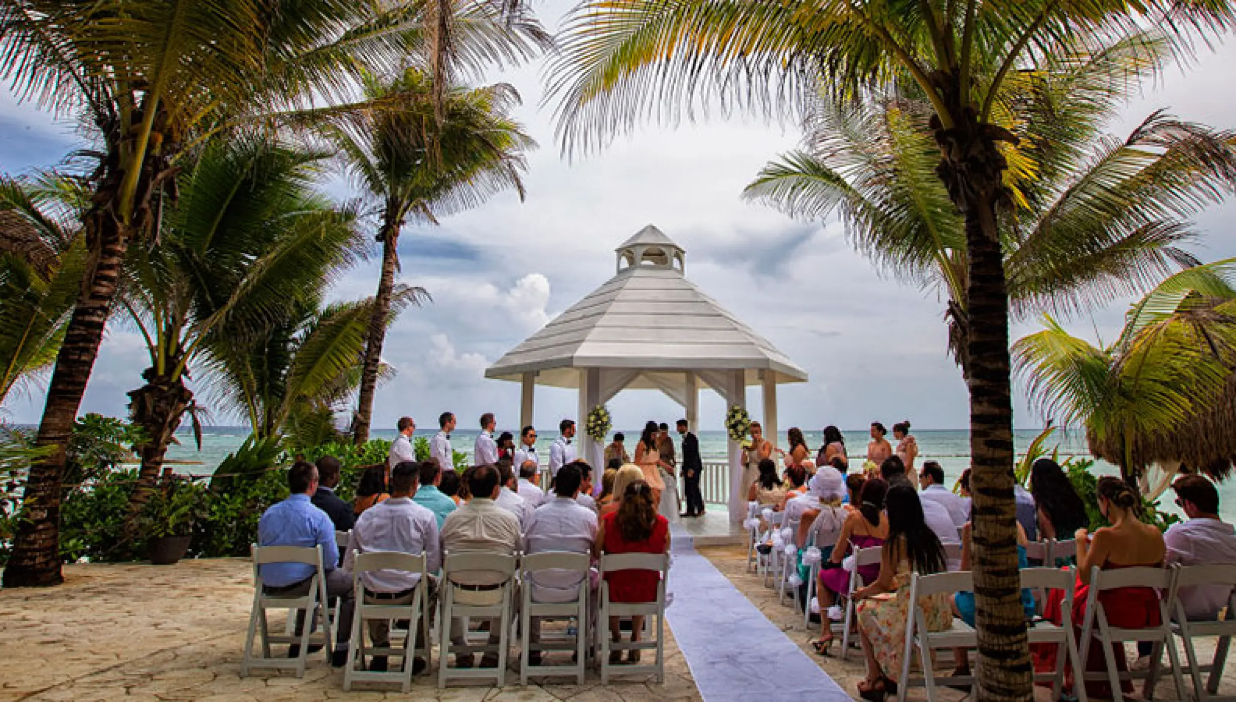 White gazebo wedding ceremony framed by palm trees at El Dorado Seaside Palms, Riviera Maya