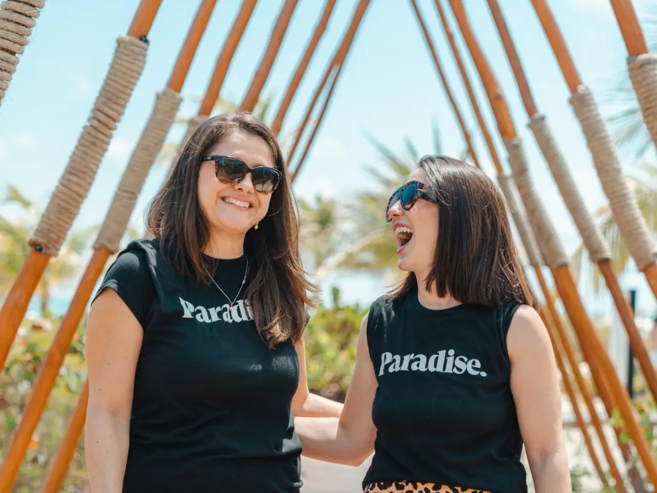 Two Paradise Weddings planners smiling under a wooden structure at a tropical resort