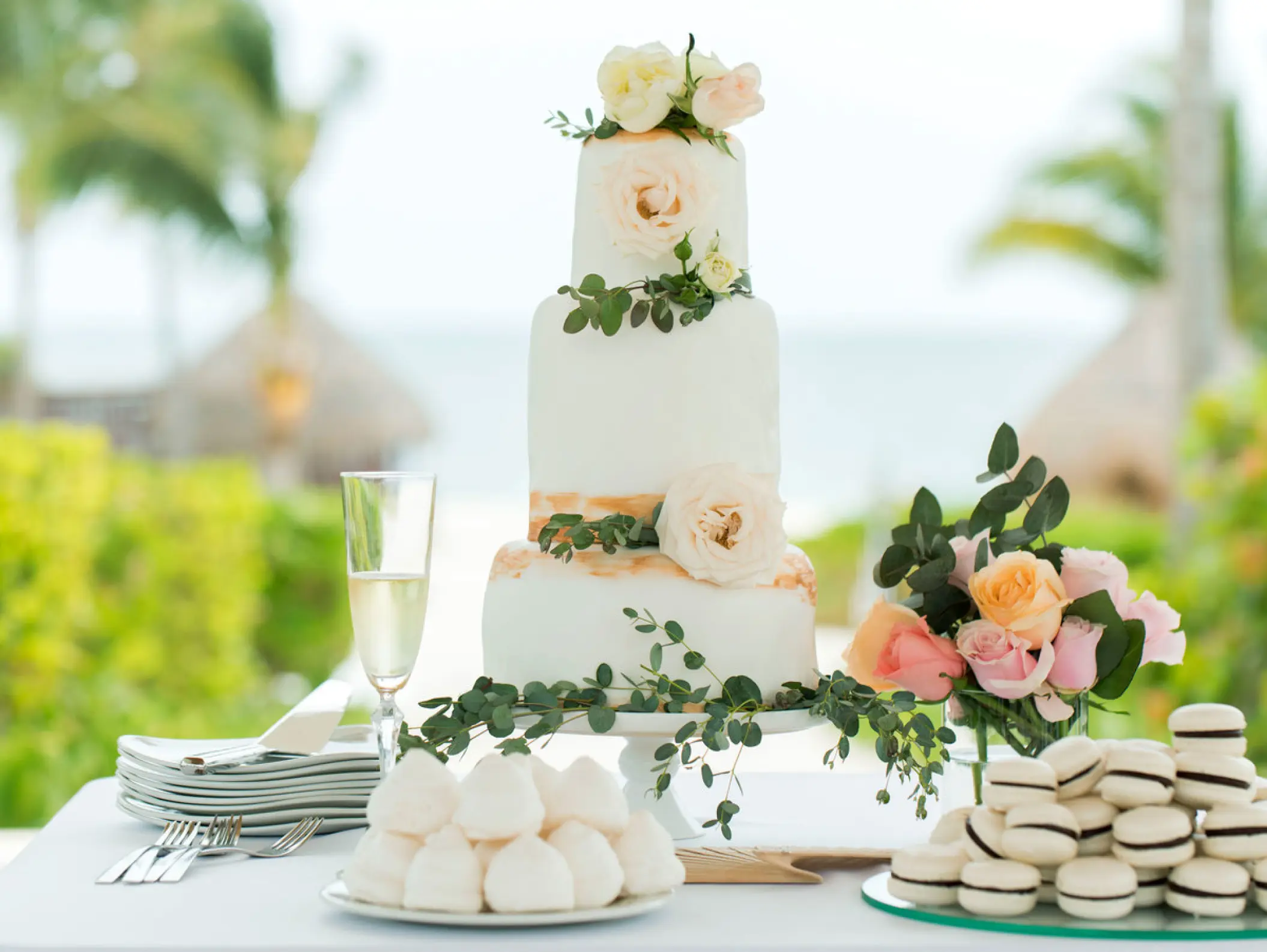 Three-tier white wedding cake with floral accents and macarons at Excellence Riviera Cancun, Riviera Maya
