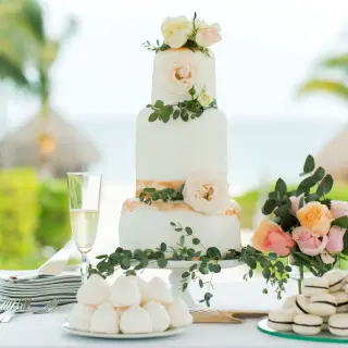Three-tier white wedding cake with floral accents and macarons at Excellence Riviera Cancun, Riviera Maya
