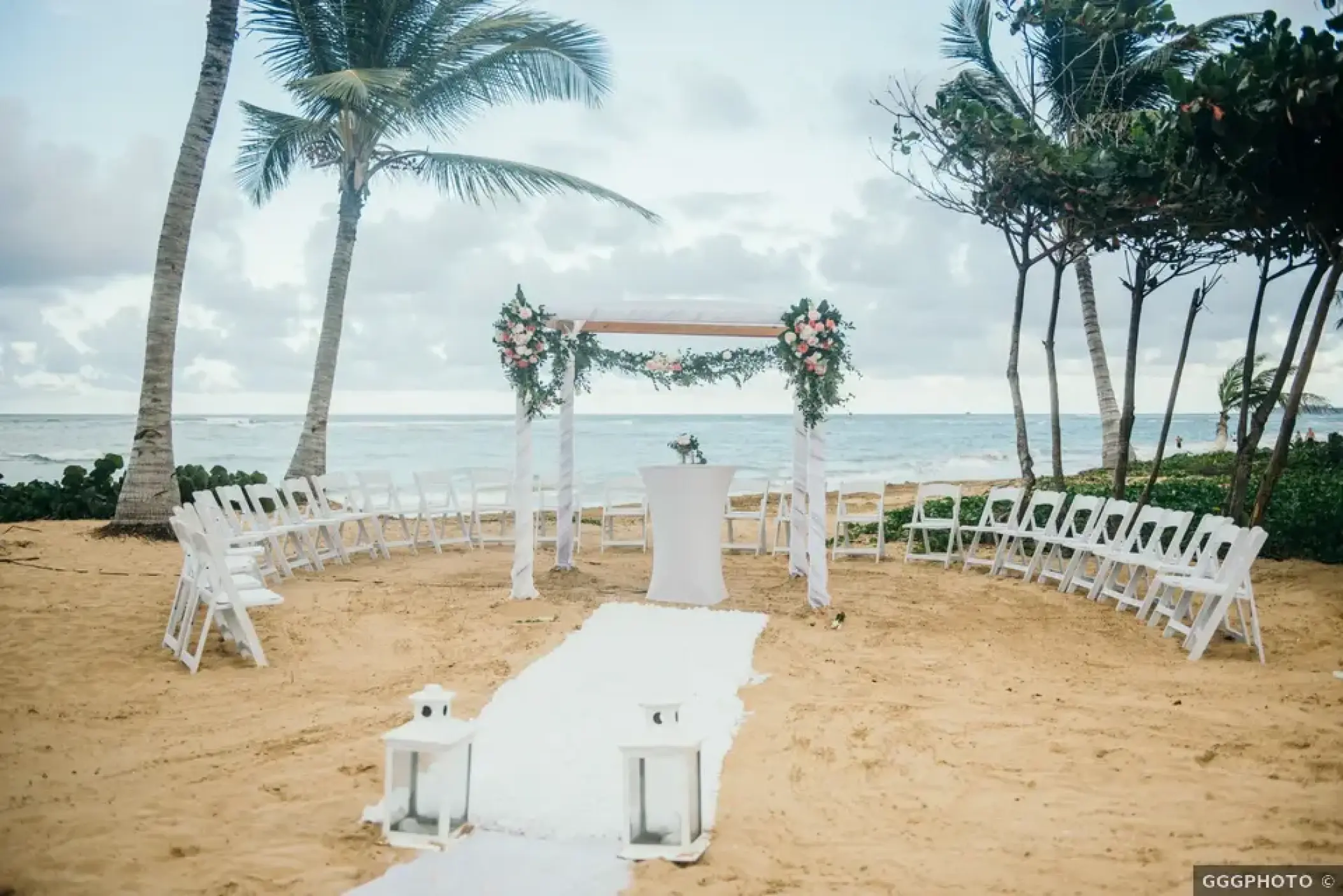 Beachfront wedding ceremony with white floral arch and circular seating at Excellence El Carmen, Punta Cana
