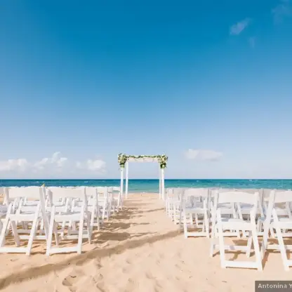 Beachfront wedding ceremony with white chairs and floral arch at Excellence El Carmen, Punta Cana