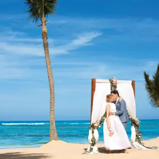 The bride and groom kissing at a beach ceremony arch at Excellence El Carmen, Punta Cana