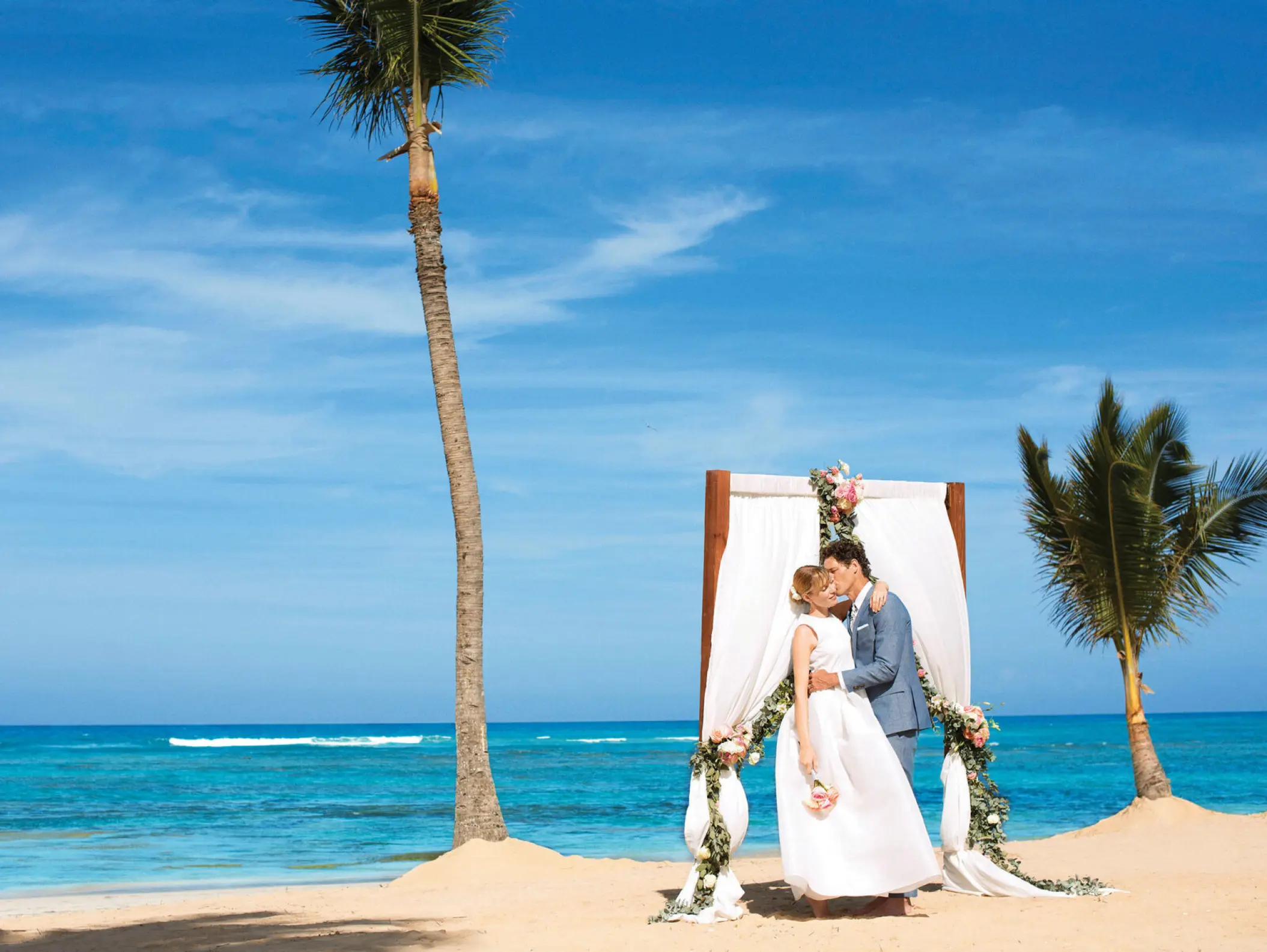 The bride and groom kissing at a beach ceremony arch at Excellence El Carmen, Punta Cana