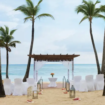 Beachfront wedding ceremony with a wooden pergola and white seating at Excellence El Carmen, Punta Cana