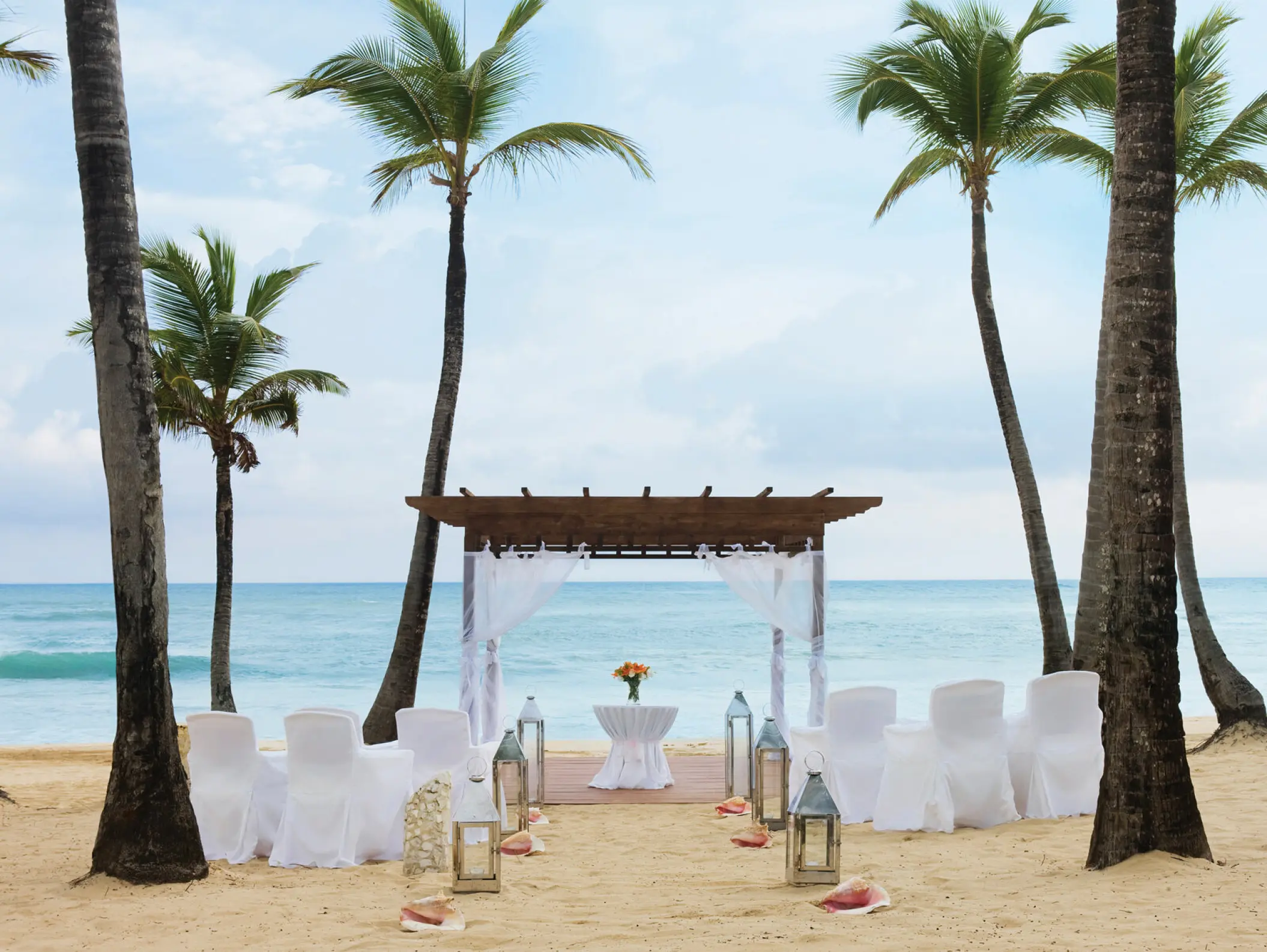 Beachfront wedding ceremony with a wooden pergola and white seating at Excellence El Carmen, Punta Cana