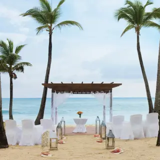 Beachfront wedding ceremony with a wooden pergola and white seating at Excellence El Carmen, Punta Cana