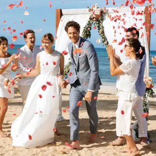 Newlyweds walking through red flower petals during a beach ceremony at Excellence El Carmen, Punta Cana