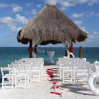 Pier wedding ceremony under a palapa with red flower petals and white chairs at Excellence Riviera Cancun