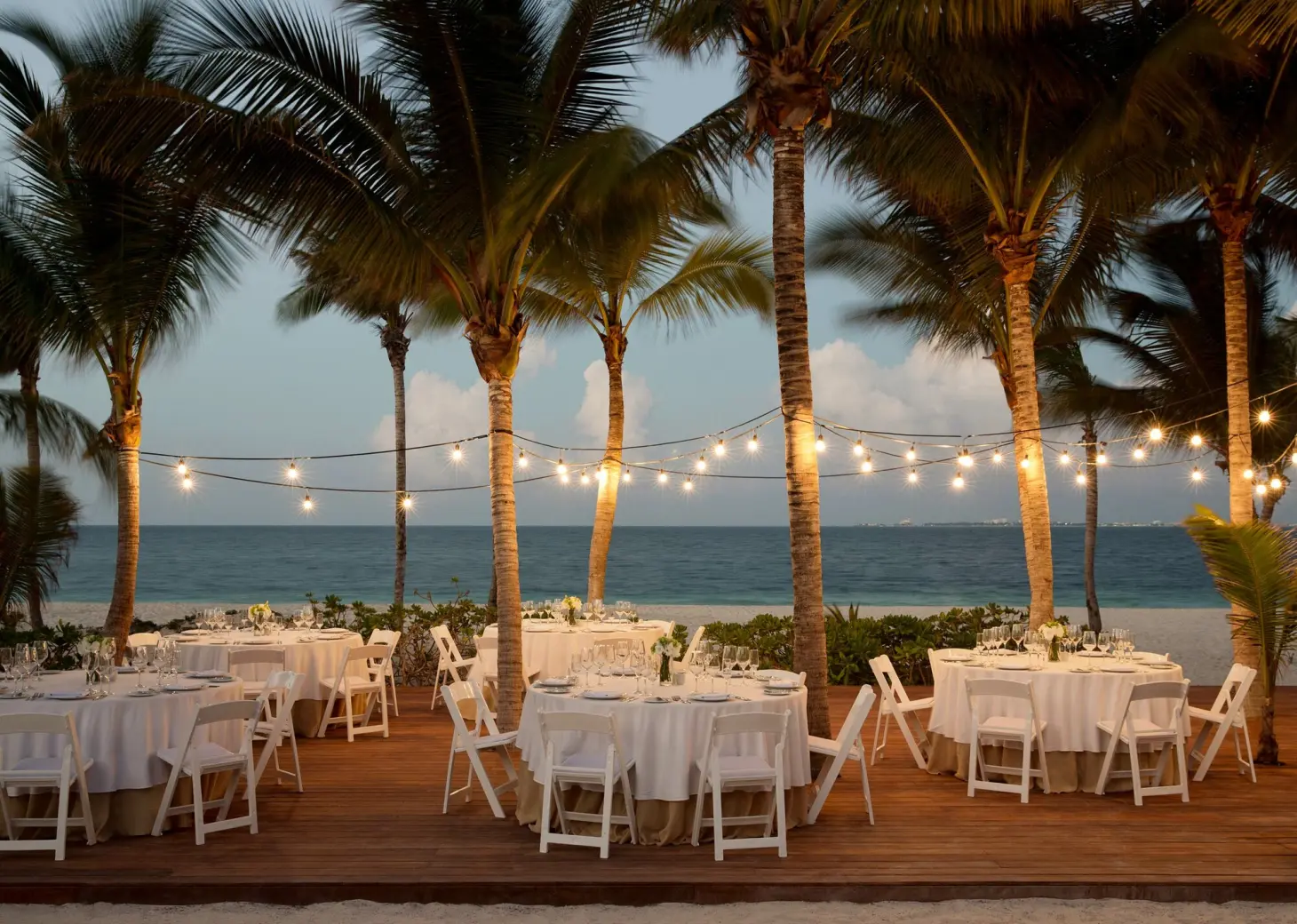 Beachfront wedding reception on a wooden deck with string lights and palm trees at Finest Playa Mujeres, Cancun