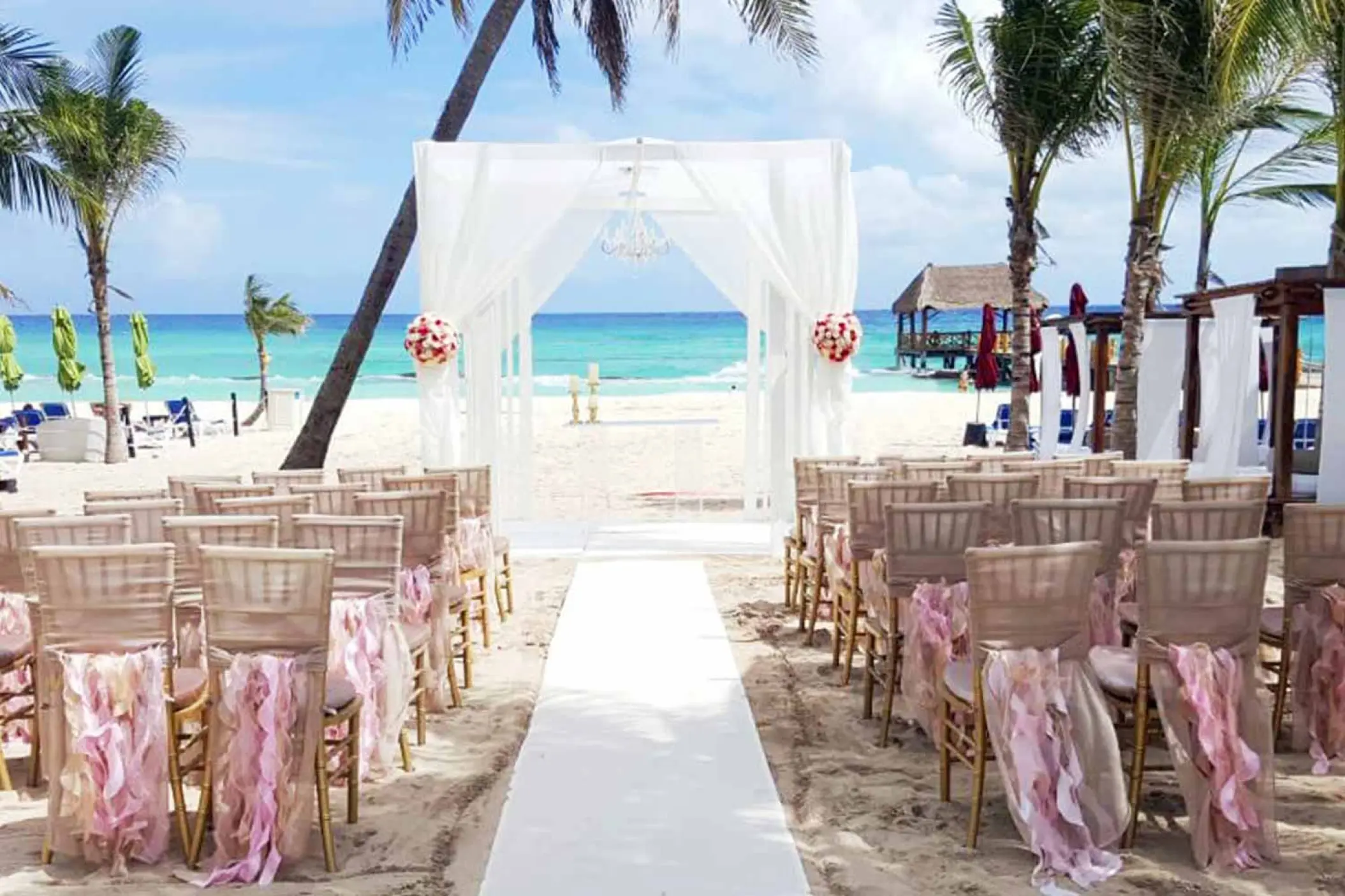 Beachfront wedding ceremony setup with white huppah and pink ruffled chairs at The Fives Beach Hotel, Playa Del Carmen