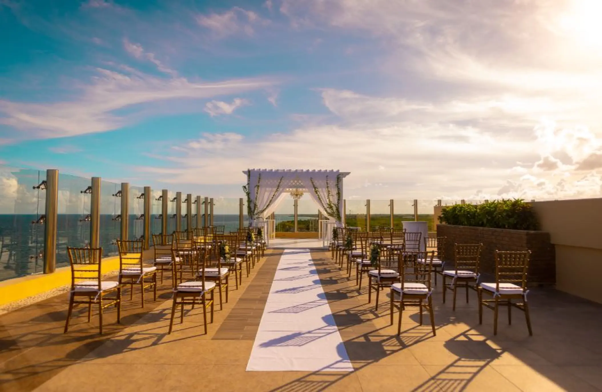 Rooftop wedding ceremony setup with white pergola and gold chairs at Generations Riviera Maya