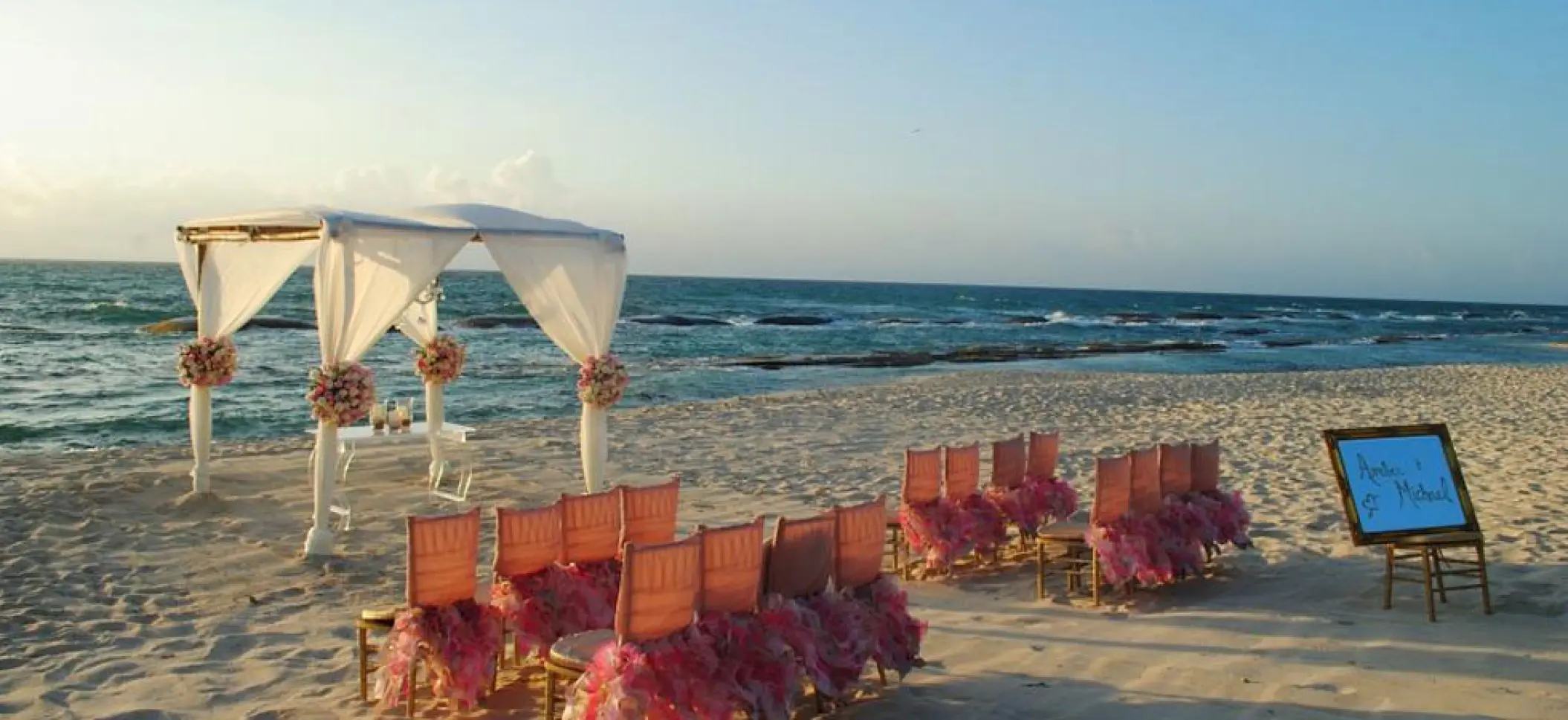 Beachfront wedding ceremony with a white canopy and pink floral decor at Generations Riviera Maya, Riviera Maya
