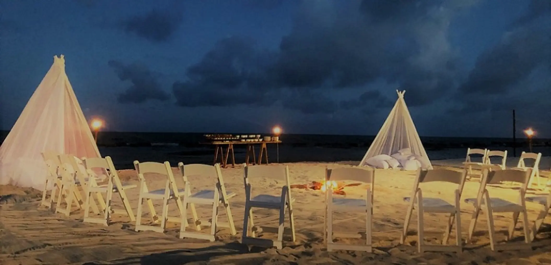 Beachfront wedding reception at night with white teepees and a fire pit at Generations Riviera Maya