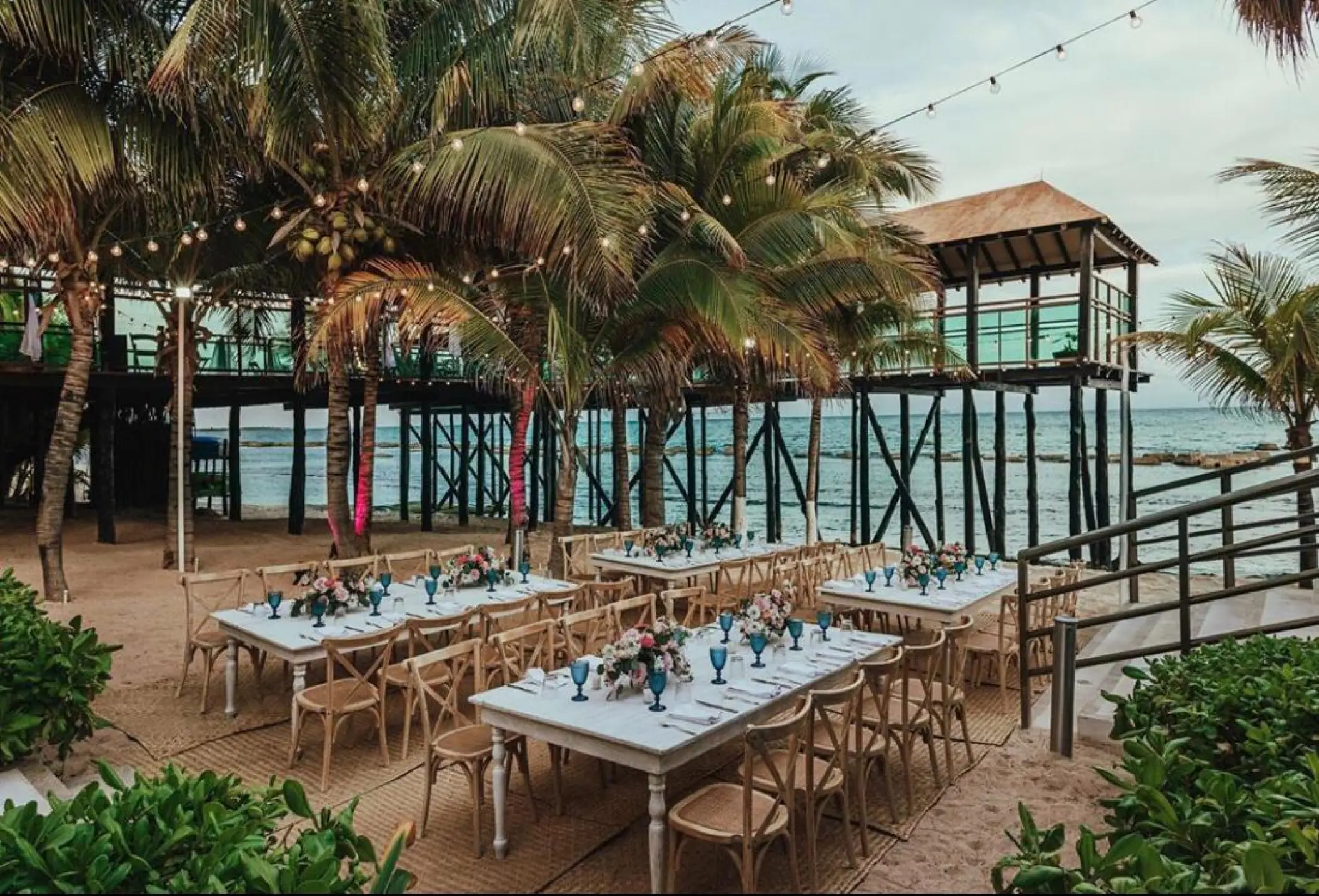 Beachfront wedding reception tables under palm trees and string lights at Generations Riviera Maya