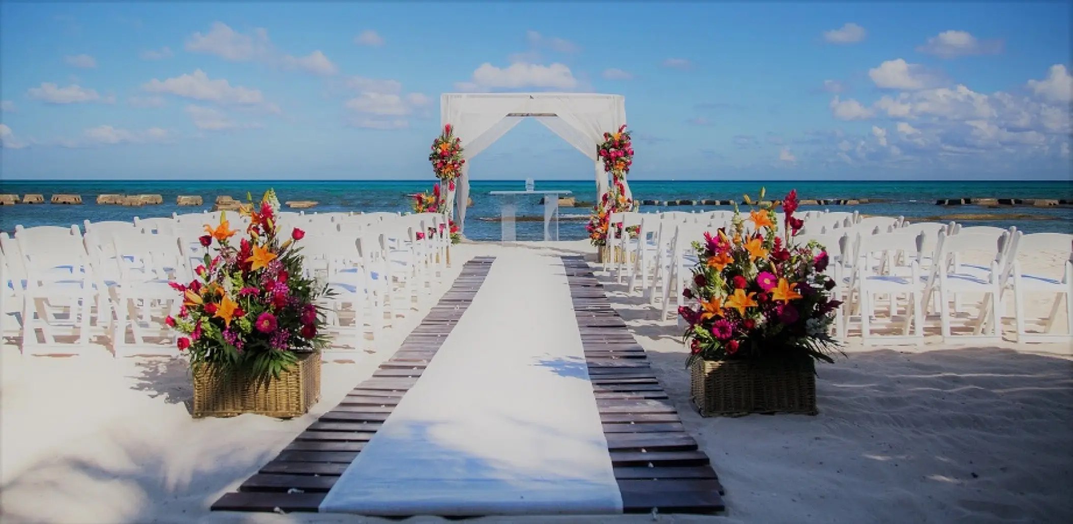 Beachfront wedding ceremony with white gazebo and colorful flowers at Generations Riviera Maya