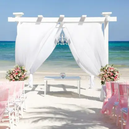 Beachfront wedding ceremony setup with a white pergola and pink chairs at Grand Palladium Colonial, Riviera Maya