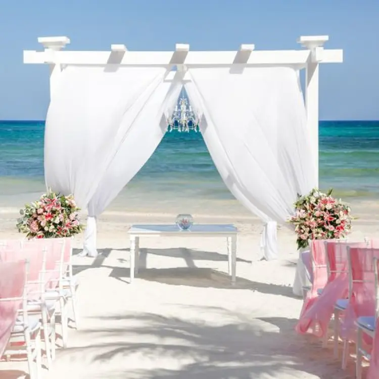 Beachfront wedding ceremony setup with a white pergola and pink chairs at Grand Palladium Colonial, Riviera Maya