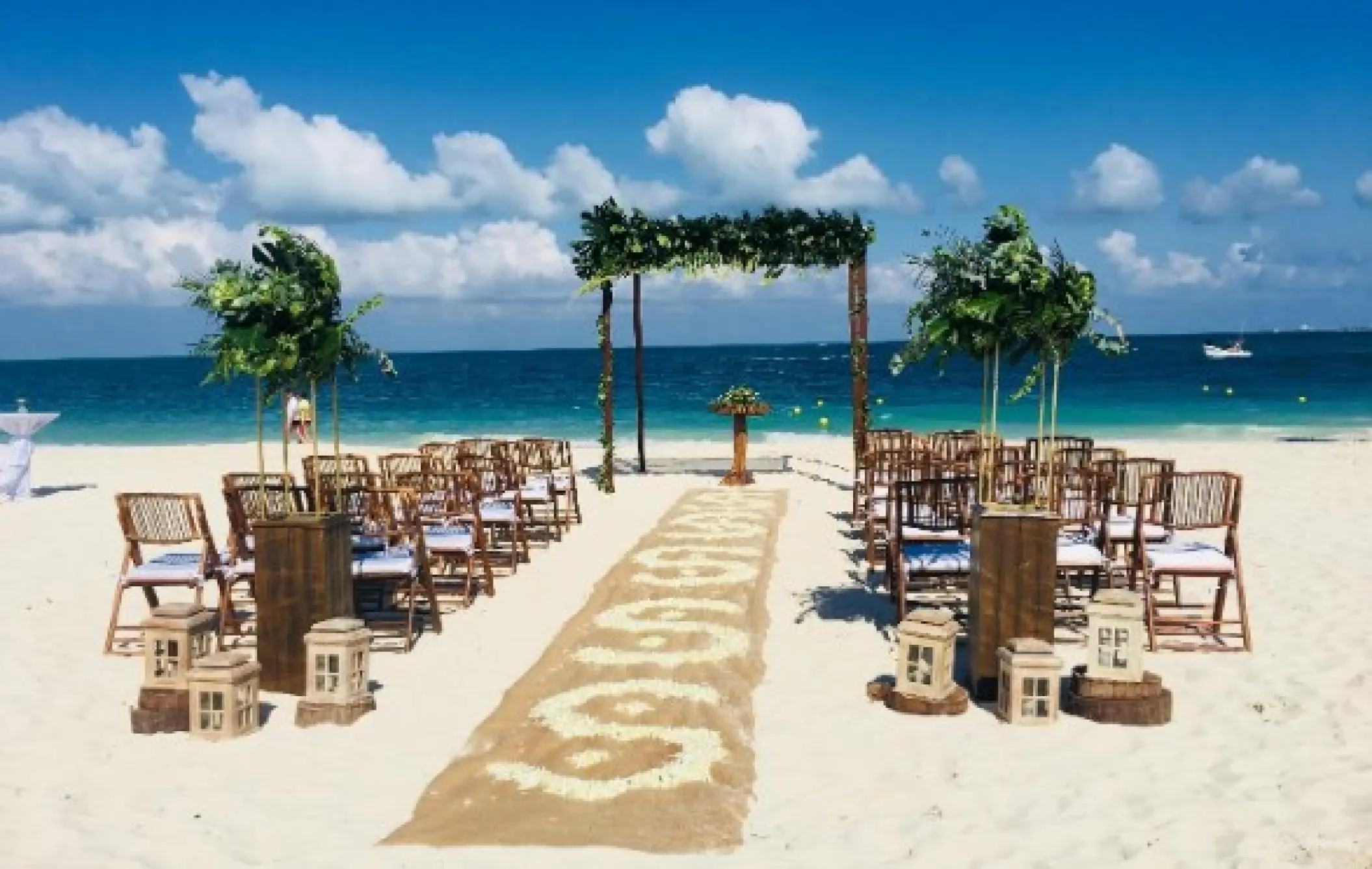 Beachfront wedding ceremony setup with greenery arch and wooden chairs at Grand Palladium Costa Mujeres, Cancun