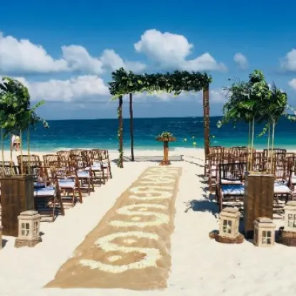Beachfront wedding ceremony setup with greenery arch and wooden chairs at Grand Palladium Costa Mujeres, Cancun