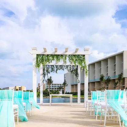 White pergola wedding ceremony setup with teal chair sashes at Grand Palladium Costa Mujeres, Cancun