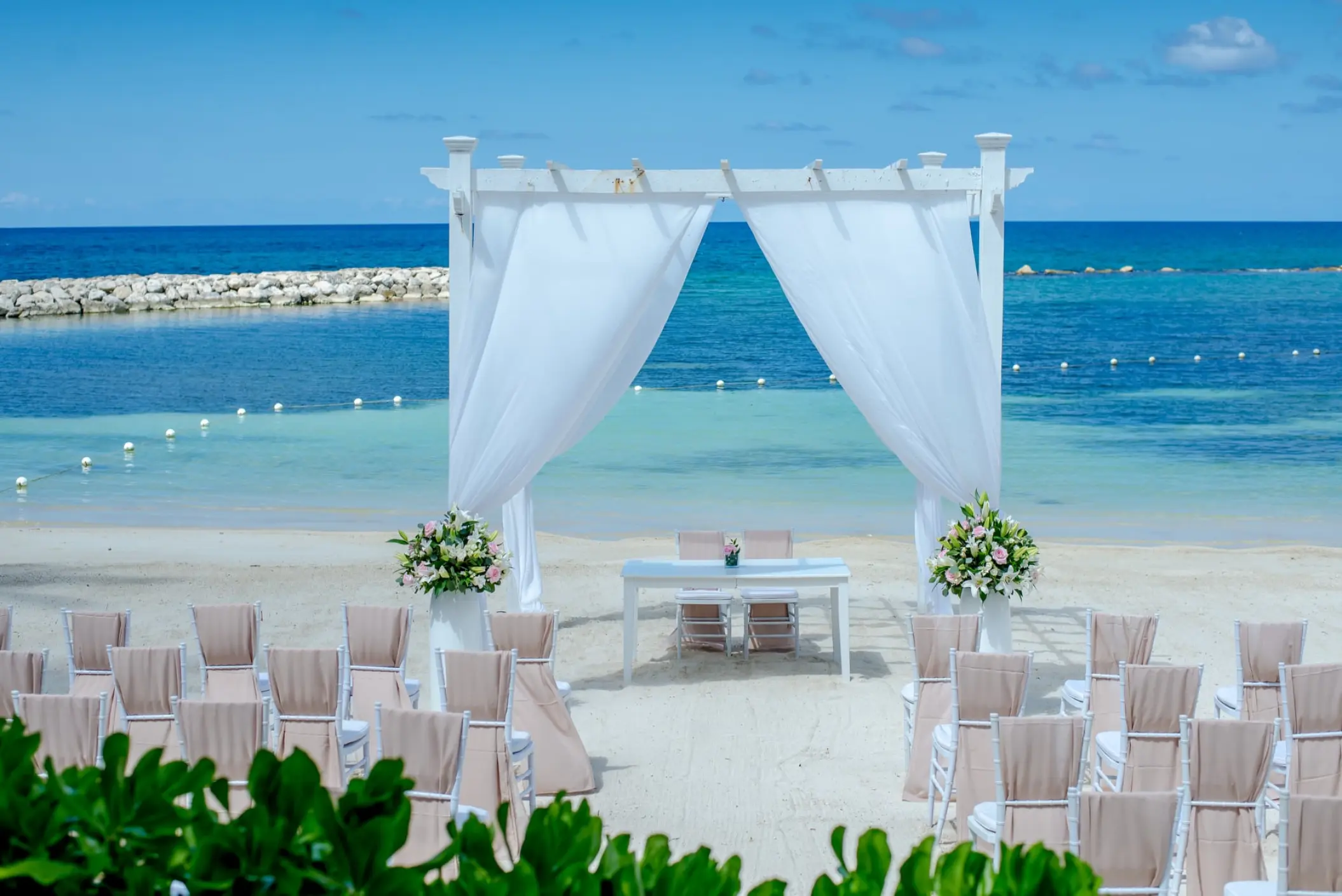 Beachfront wedding ceremony setup with a white pergola and draped fabric at Grand Palladium Lady Hamilton, Ocho Rios
