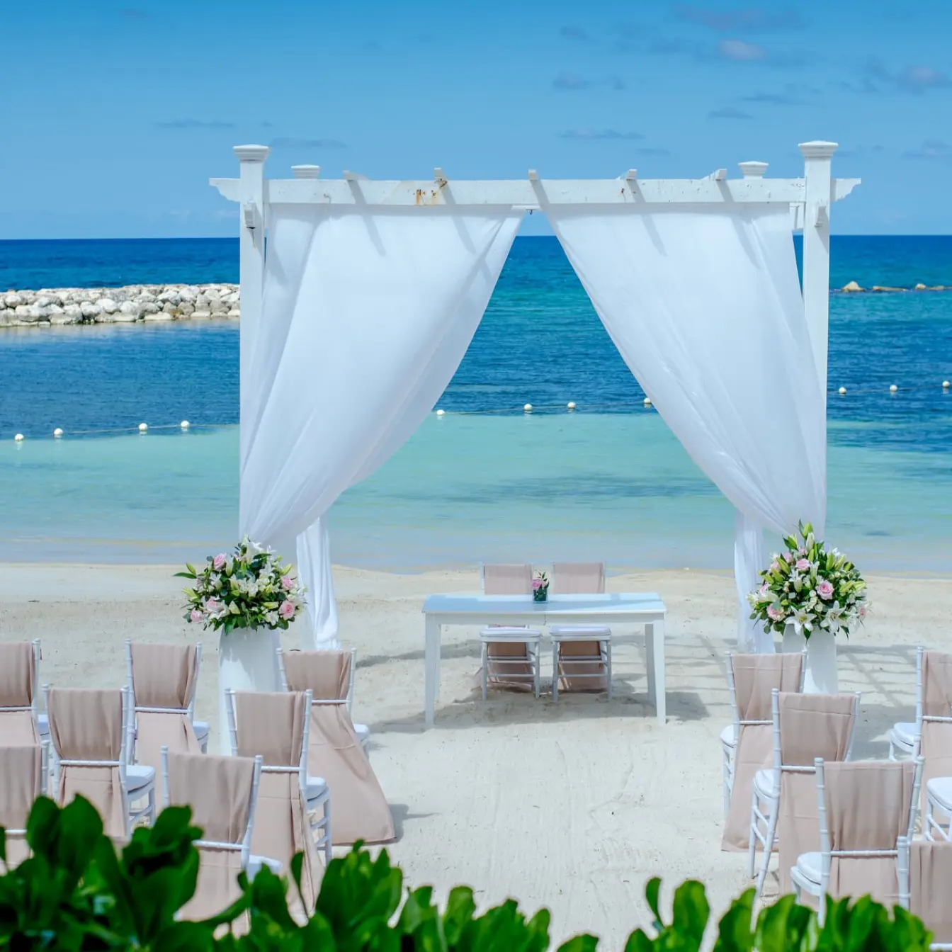Beachfront wedding ceremony setup with a white pergola and draped fabric at Grand Palladium Lady Hamilton, Ocho Rios