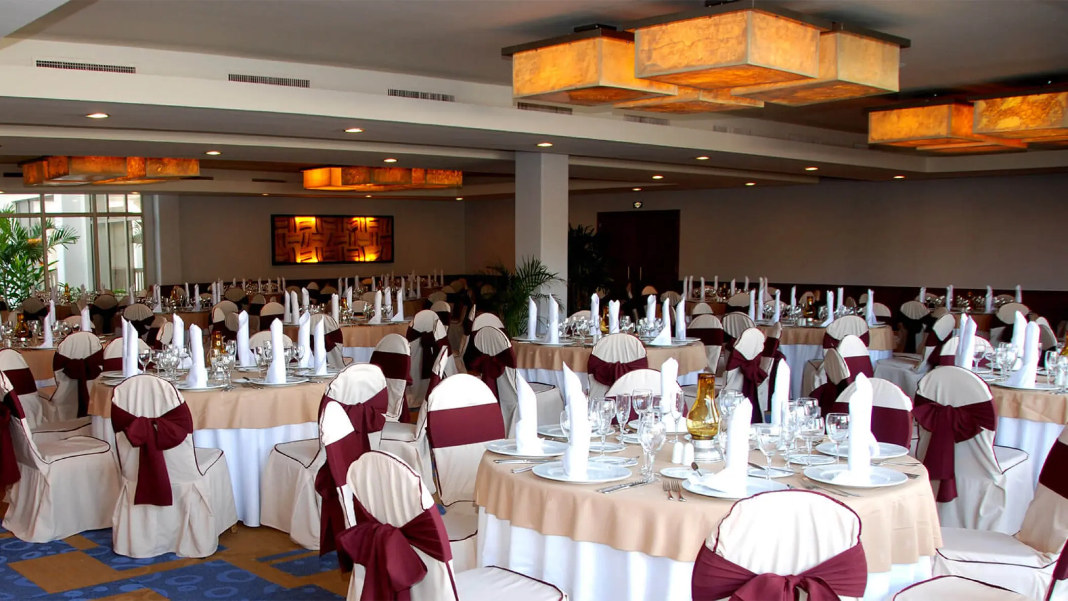 Indoor wedding reception with round tables and burgundy chair sashes at Grand Riviera Princess, Playa Del Carmen