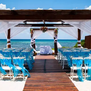 Beachfront wedding ceremony with blue-draped chairs under a wooden gazebo at Grand Riviera Princess, Playa Del Carmen