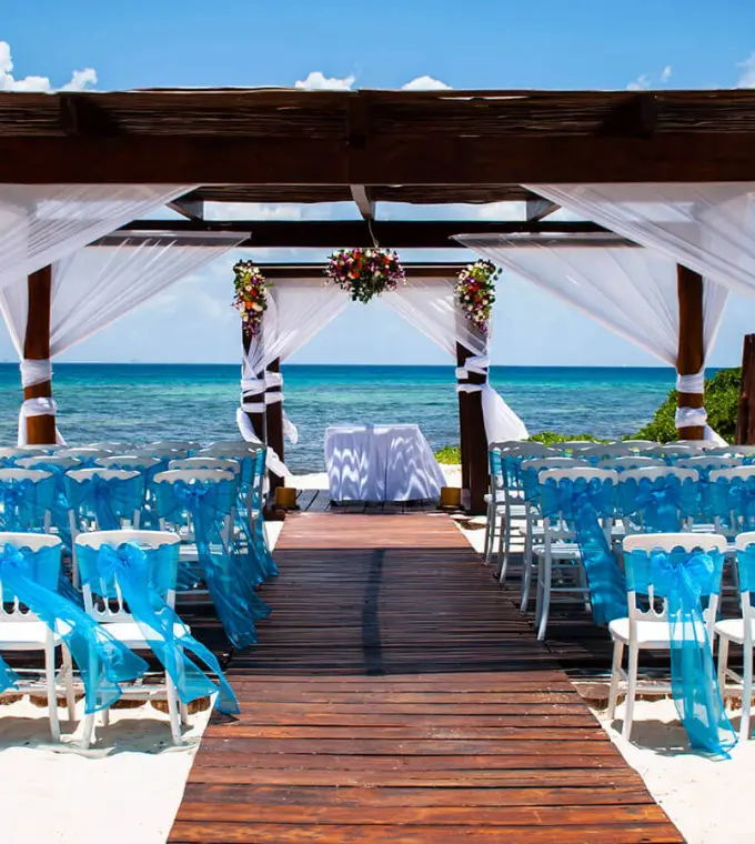 Beachfront wedding ceremony with blue-draped chairs under a wooden gazebo at Grand Riviera Princess, Playa Del Carmen