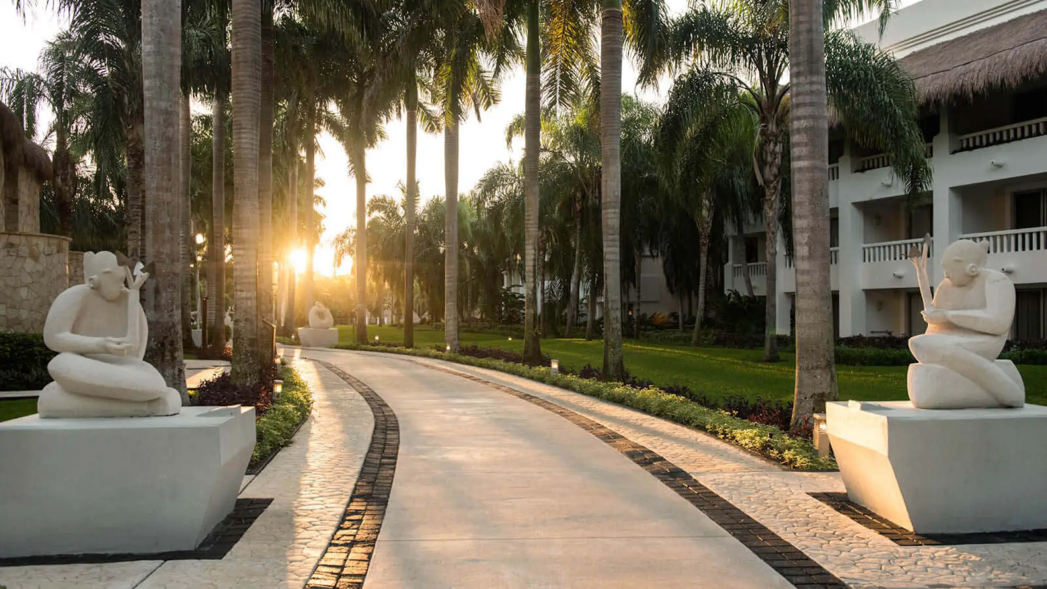 Sunlit walkway with stone statues and palm trees at Grand Riviera Princess, Playa Del Carmen