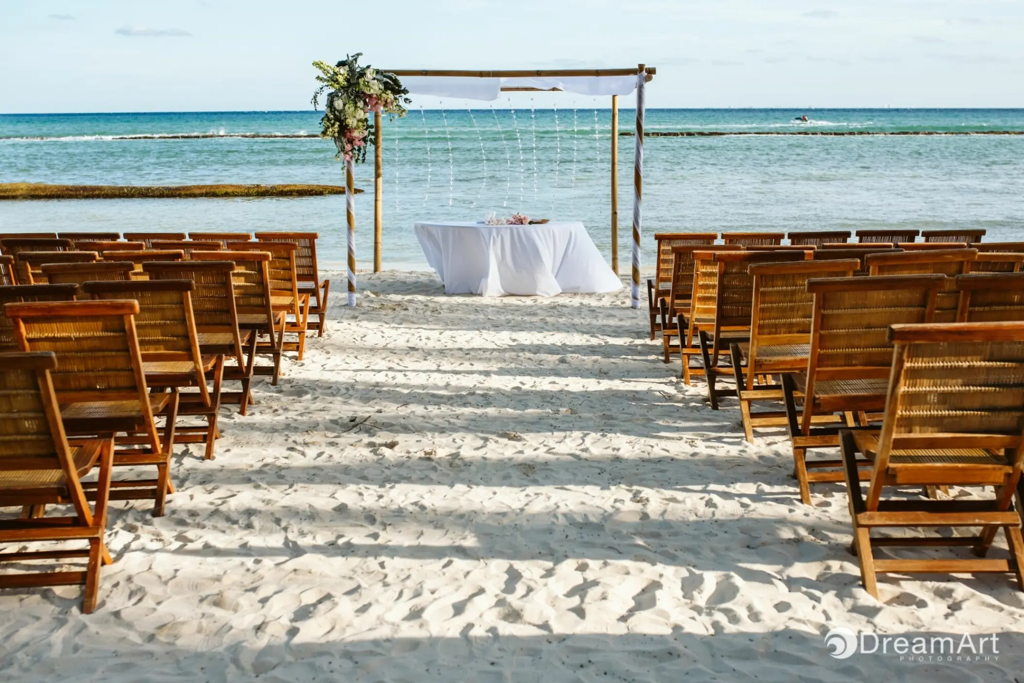 Beachfront wedding ceremony with wooden chairs and floral arch at Grand Velas Riviera Maya, Riviera Maya